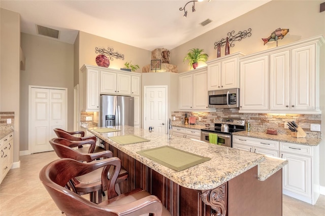 kitchen featuring appliances with stainless steel finishes, light stone countertops, an island with sink, and a breakfast bar