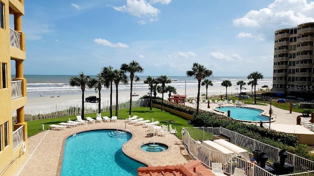 pool featuring a water view, a hot tub, fence, and a beach view