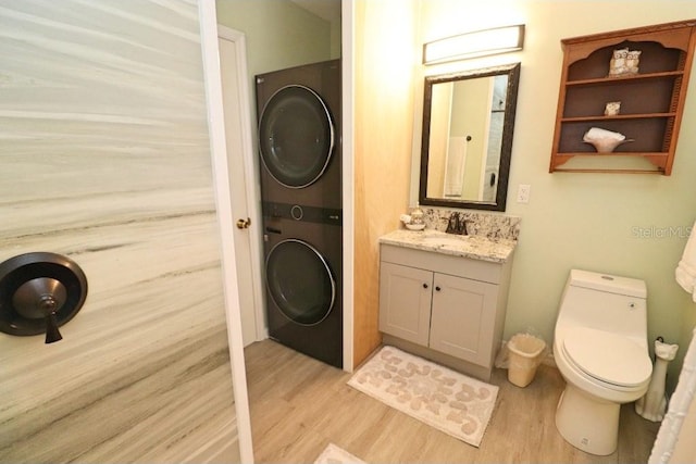 bathroom featuring stacked washer / drying machine, hardwood / wood-style flooring, vanity, and toilet