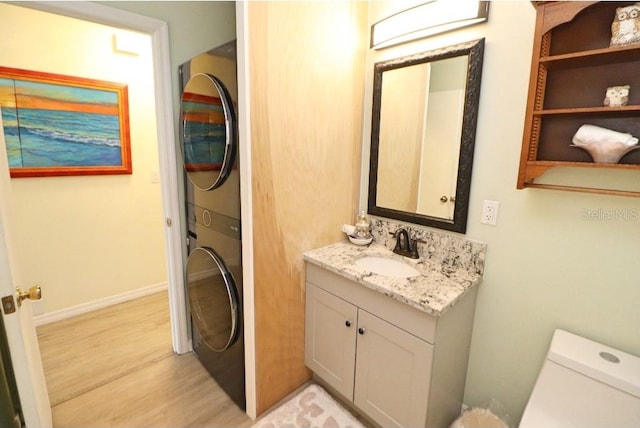 bathroom featuring wood-type flooring, vanity, stacked washer / drying machine, and toilet