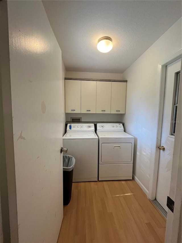 clothes washing area featuring a textured ceiling, washer and dryer, light hardwood / wood-style flooring, and cabinets