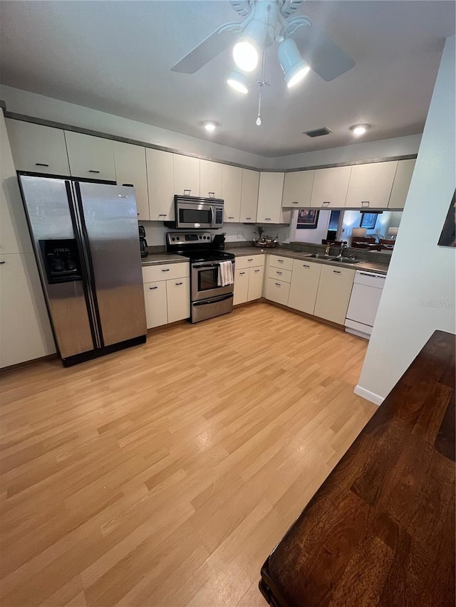 kitchen with light wood-type flooring, ceiling fan, sink, white cabinetry, and appliances with stainless steel finishes