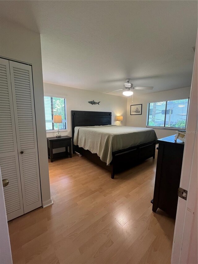 bedroom with ceiling fan, a closet, light hardwood / wood-style floors, and a textured ceiling