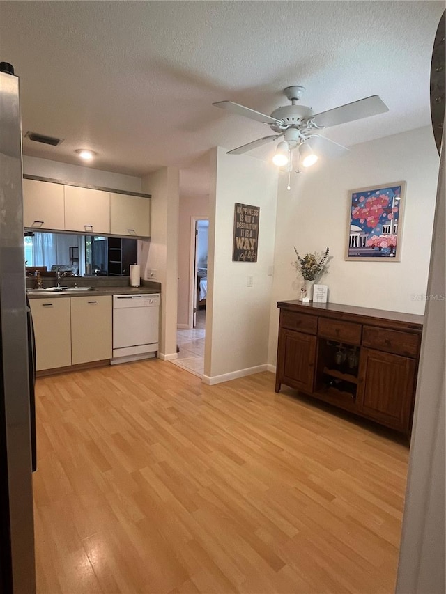 kitchen featuring light wood-type flooring, ceiling fan, cream cabinets, white dishwasher, and a textured ceiling