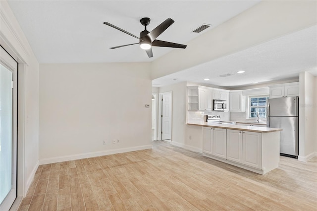 kitchen featuring appliances with stainless steel finishes, white cabinets, kitchen peninsula, light wood-type flooring, and ceiling fan