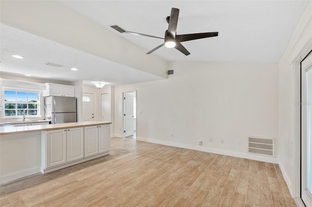 kitchen featuring light wood-type flooring, white cabinetry, vaulted ceiling, stainless steel refrigerator, and ceiling fan