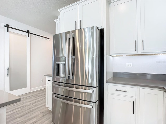 kitchen with stainless steel fridge, a textured ceiling, a barn door, light hardwood / wood-style flooring, and white cabinets