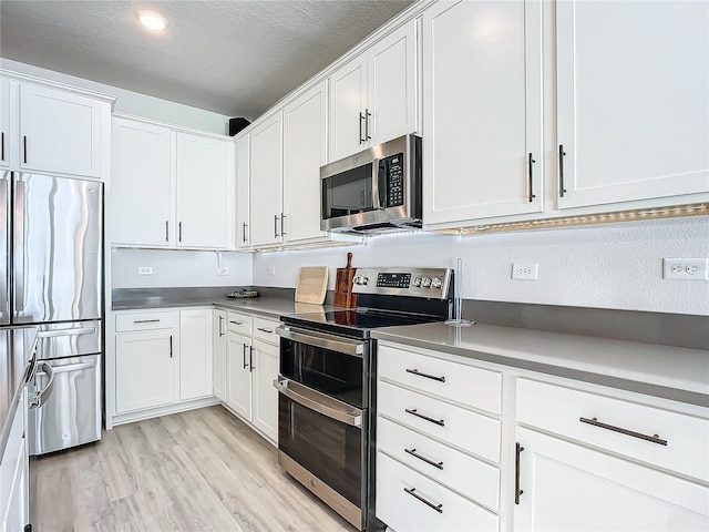 kitchen featuring white cabinets, light wood-type flooring, a textured ceiling, and appliances with stainless steel finishes