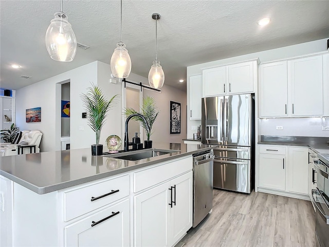 kitchen with a barn door, white cabinetry, stainless steel appliances, and hanging light fixtures