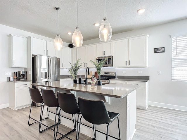 kitchen with appliances with stainless steel finishes, a textured ceiling, pendant lighting, white cabinetry, and an island with sink