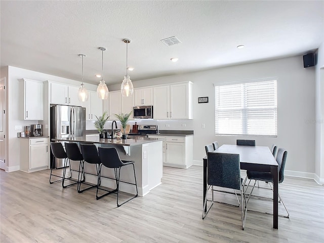 kitchen featuring appliances with stainless steel finishes, light wood-type flooring, decorative light fixtures, and white cabinetry