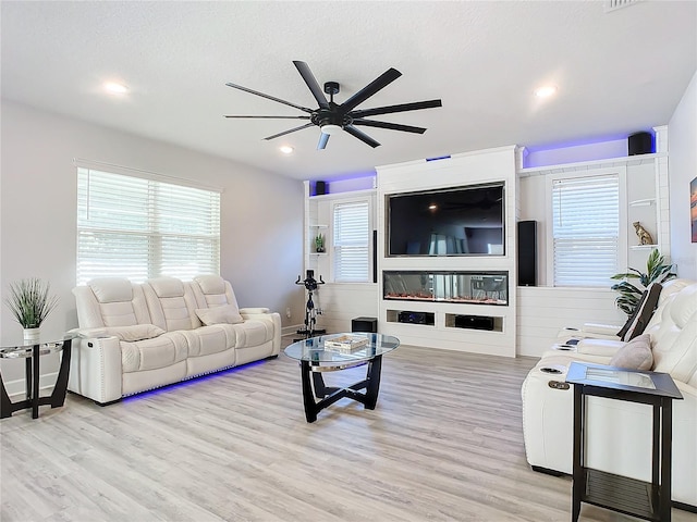 living room with a textured ceiling, light wood-type flooring, and ceiling fan