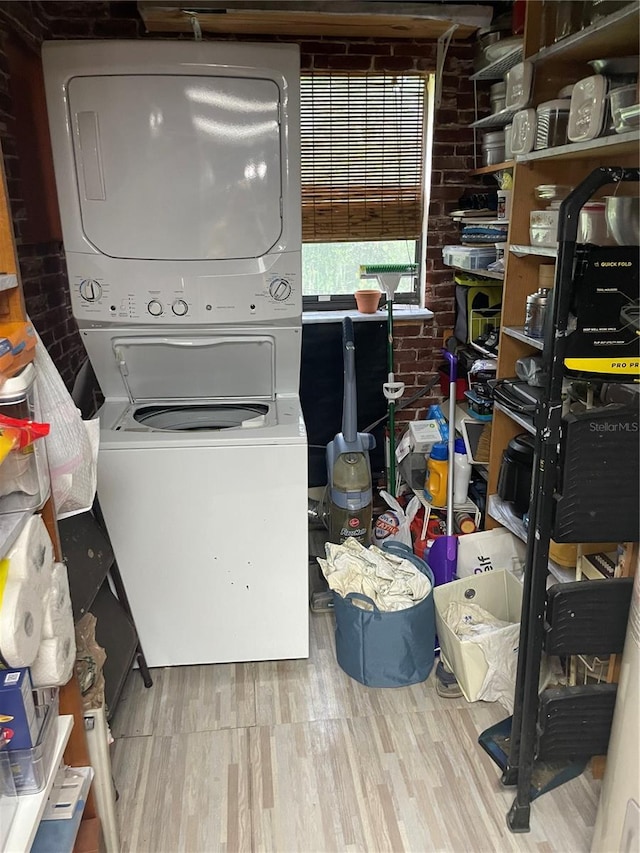 laundry room with brick wall, light hardwood / wood-style floors, and stacked washer / drying machine