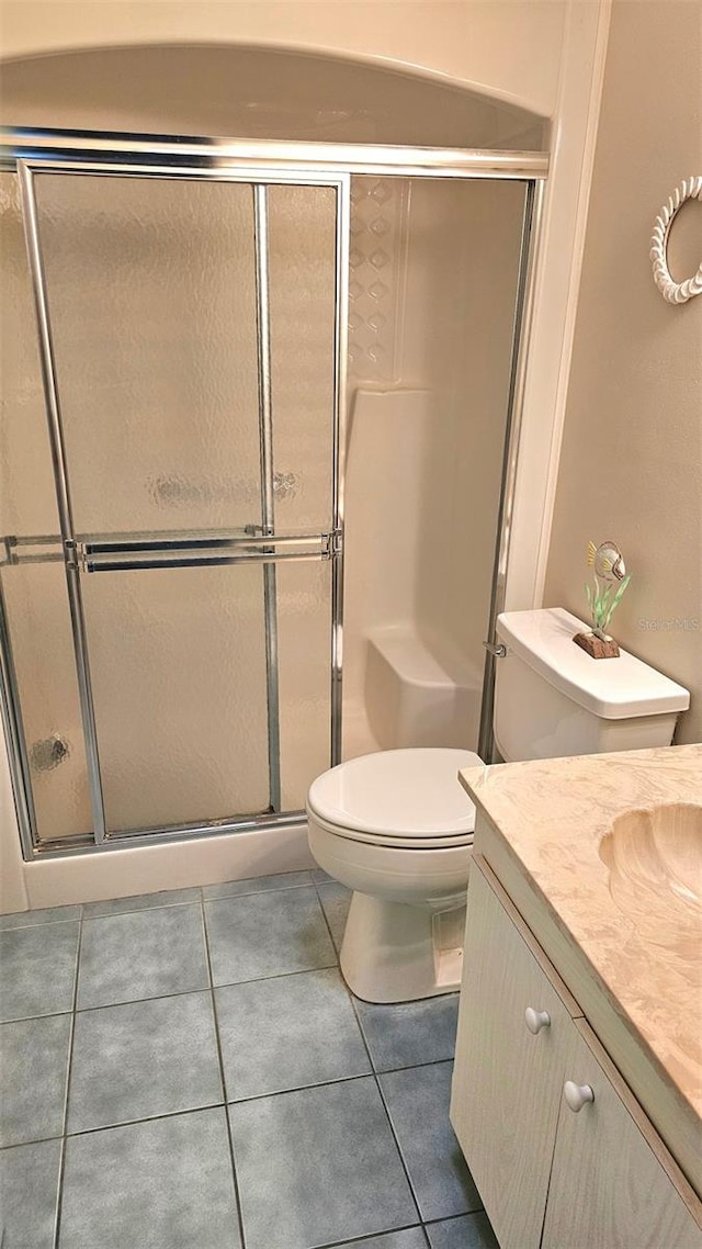 bathroom with tile patterned floors, vanity, toilet, and a shower with shower door