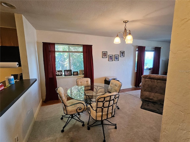 carpeted dining area with a notable chandelier and a textured ceiling