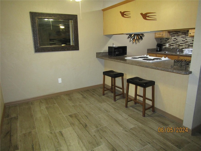 kitchen featuring a kitchen breakfast bar, tasteful backsplash, white stovetop, light wood-type flooring, and sink