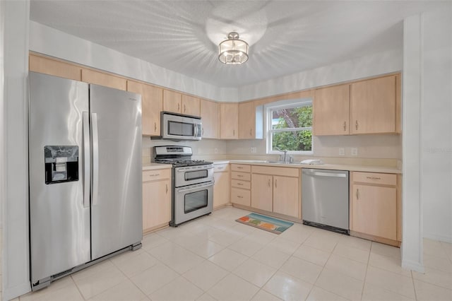 kitchen with sink, light tile patterned floors, appliances with stainless steel finishes, a textured ceiling, and light brown cabinets