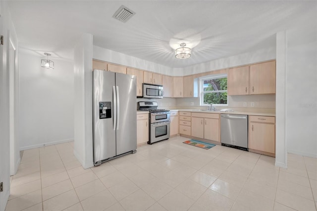 kitchen with stainless steel appliances, sink, light tile patterned floors, and light brown cabinetry