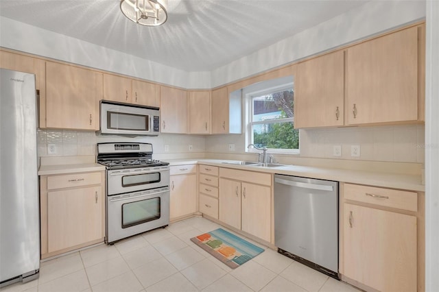 kitchen with appliances with stainless steel finishes, sink, light tile patterned floors, and light brown cabinetry