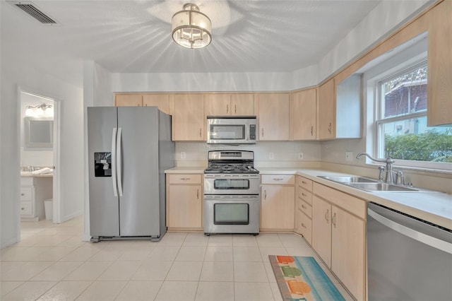 kitchen with stainless steel appliances, light brown cabinetry, sink, and light tile patterned floors