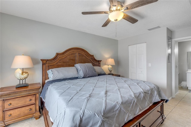 bedroom featuring ceiling fan, light tile patterned floors, a textured ceiling, a closet, and ensuite bath