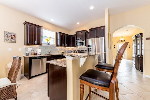 kitchen with light stone countertops, a kitchen island, lofted ceiling, light tile patterned floors, and appliances with stainless steel finishes