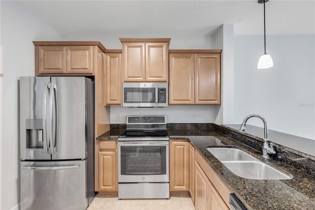 kitchen with dark stone counters, light brown cabinets, sink, stainless steel appliances, and hanging light fixtures