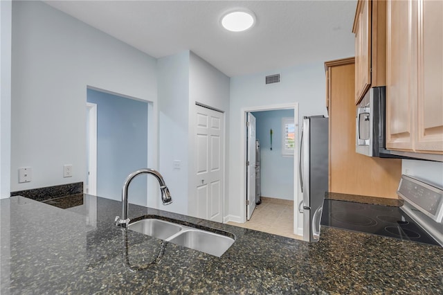 kitchen featuring stainless steel appliances, dark stone countertops, sink, and light tile patterned floors