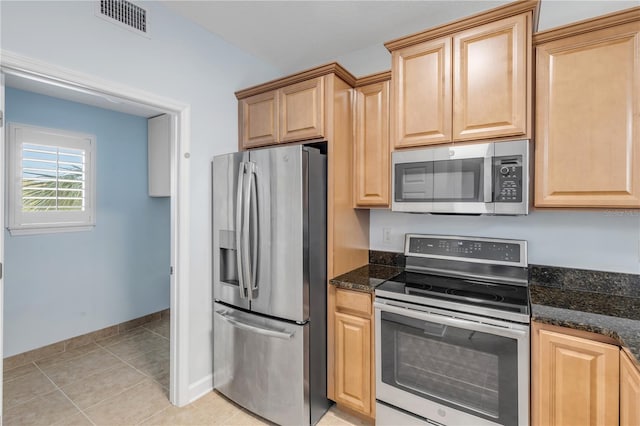 kitchen featuring appliances with stainless steel finishes, dark stone countertops, light tile patterned flooring, and light brown cabinets