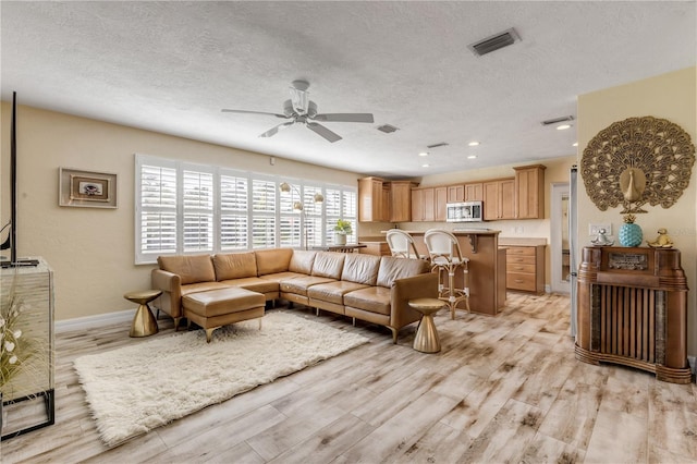 living room with ceiling fan, a textured ceiling, and light wood-type flooring