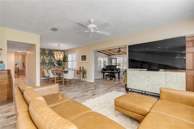 living room featuring light hardwood / wood-style flooring, a textured ceiling, and ceiling fan with notable chandelier