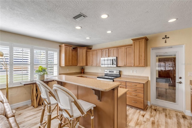 kitchen featuring a breakfast bar area, a textured ceiling, light hardwood / wood-style flooring, and stainless steel appliances