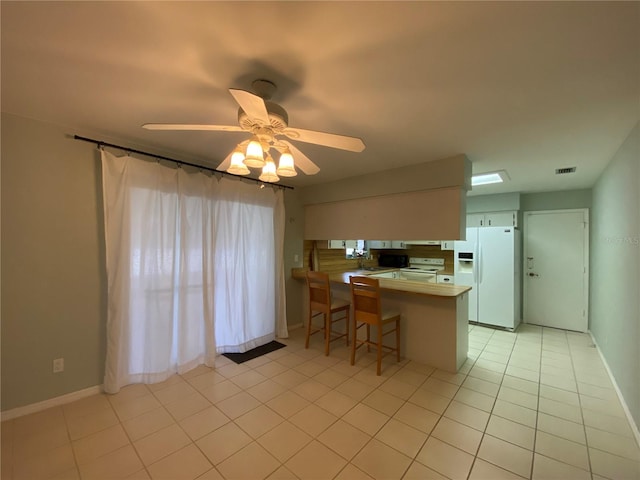 kitchen with ceiling fan, a breakfast bar area, white fridge with ice dispenser, kitchen peninsula, and light tile patterned floors