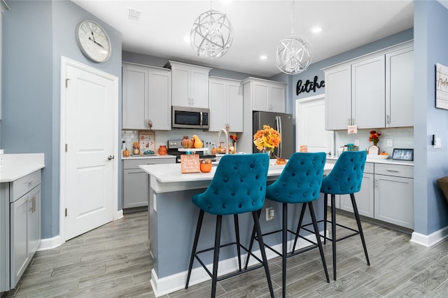 kitchen with tasteful backsplash, a kitchen breakfast bar, stainless steel appliances, pendant lighting, and gray cabinets