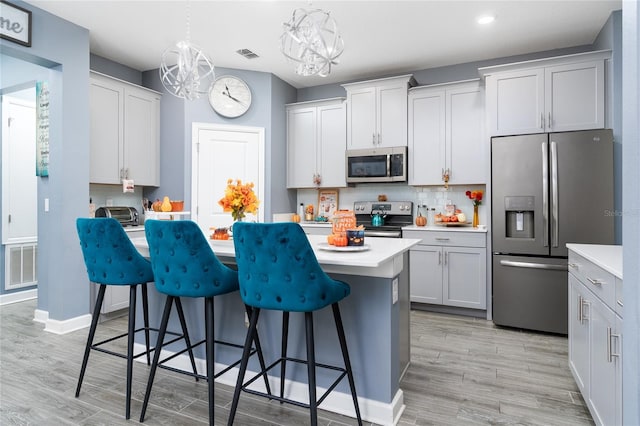 kitchen featuring light hardwood / wood-style floors, stainless steel appliances, a kitchen breakfast bar, and hanging light fixtures