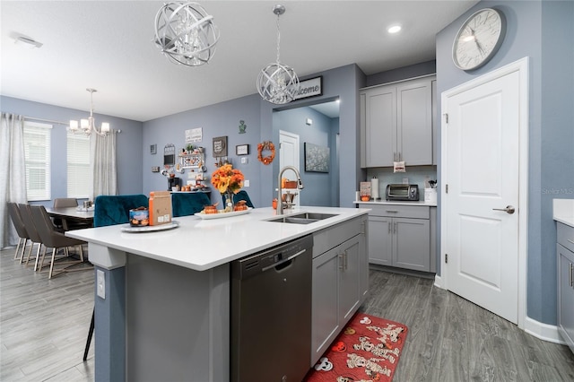 kitchen with hanging light fixtures, an island with sink, dishwasher, gray cabinets, and sink