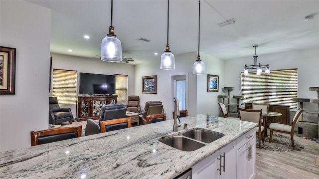 kitchen with hanging light fixtures, light stone counters, white cabinetry, light hardwood / wood-style flooring, and sink