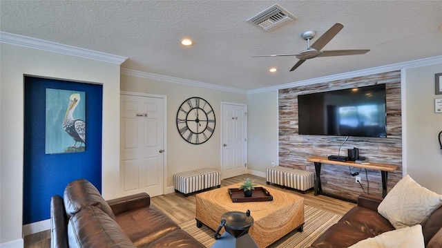 living area with a textured ceiling, wood finished floors, visible vents, baseboards, and crown molding