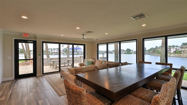 dining room featuring a water view, light wood-type flooring, visible vents, and a textured ceiling