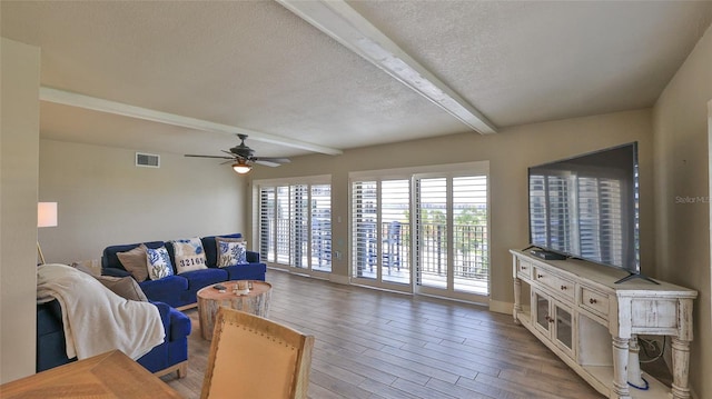 living area with visible vents, ceiling fan, wood finished floors, a textured ceiling, and beam ceiling