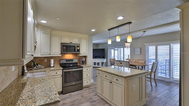 kitchen featuring wood finish floors, cream cabinetry, tasteful backsplash, appliances with stainless steel finishes, and a sink