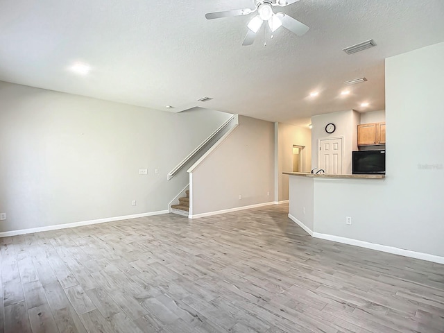 unfurnished living room featuring light hardwood / wood-style floors, a textured ceiling, and ceiling fan