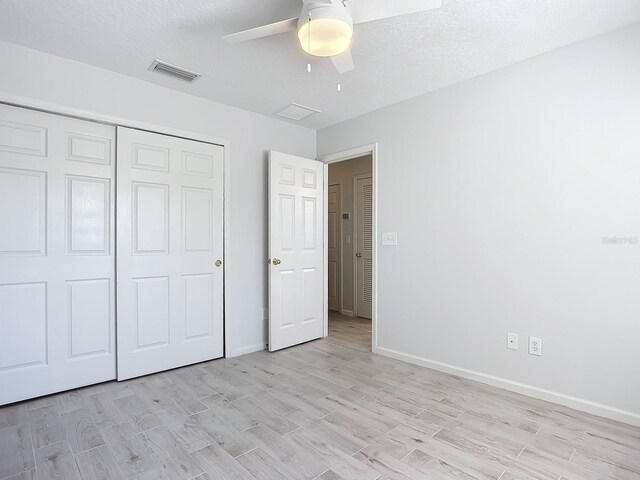 unfurnished bedroom with light hardwood / wood-style floors, a closet, a textured ceiling, and ceiling fan