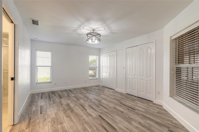 unfurnished bedroom with light hardwood / wood-style floors, a textured ceiling, and two closets