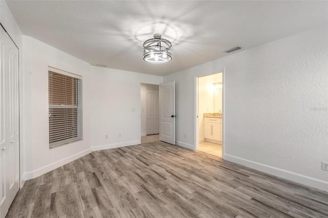 unfurnished bedroom with a closet, ensuite bathroom, and light hardwood / wood-style floors