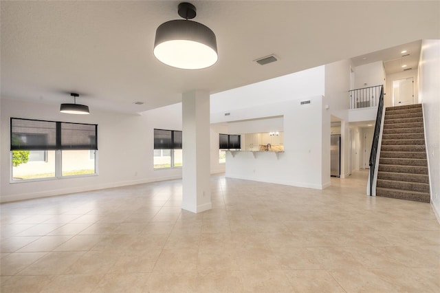 2266 Hawks Cove Cir, New Smyrna Beach, FL 32168 - unfurnished living room featuring plenty of natural light, stairway, light tile patterned floors, baseboards, and a high ceiling