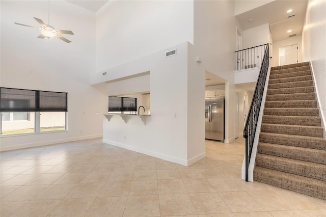 unfurnished living room featuring sink, ceiling fan, a towering ceiling, and light tile patterned floors