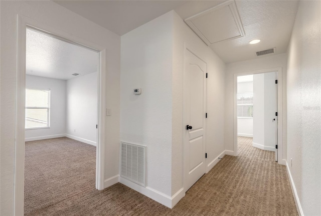 corridor with light carpet and a textured ceiling