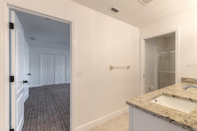 bathroom with vanity, a shower with shower door, a textured ceiling, and tile patterned floors