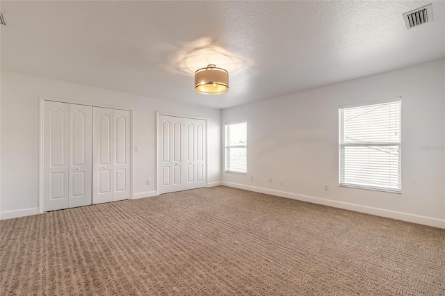 unfurnished bedroom featuring a textured ceiling, two closets, and carpet flooring